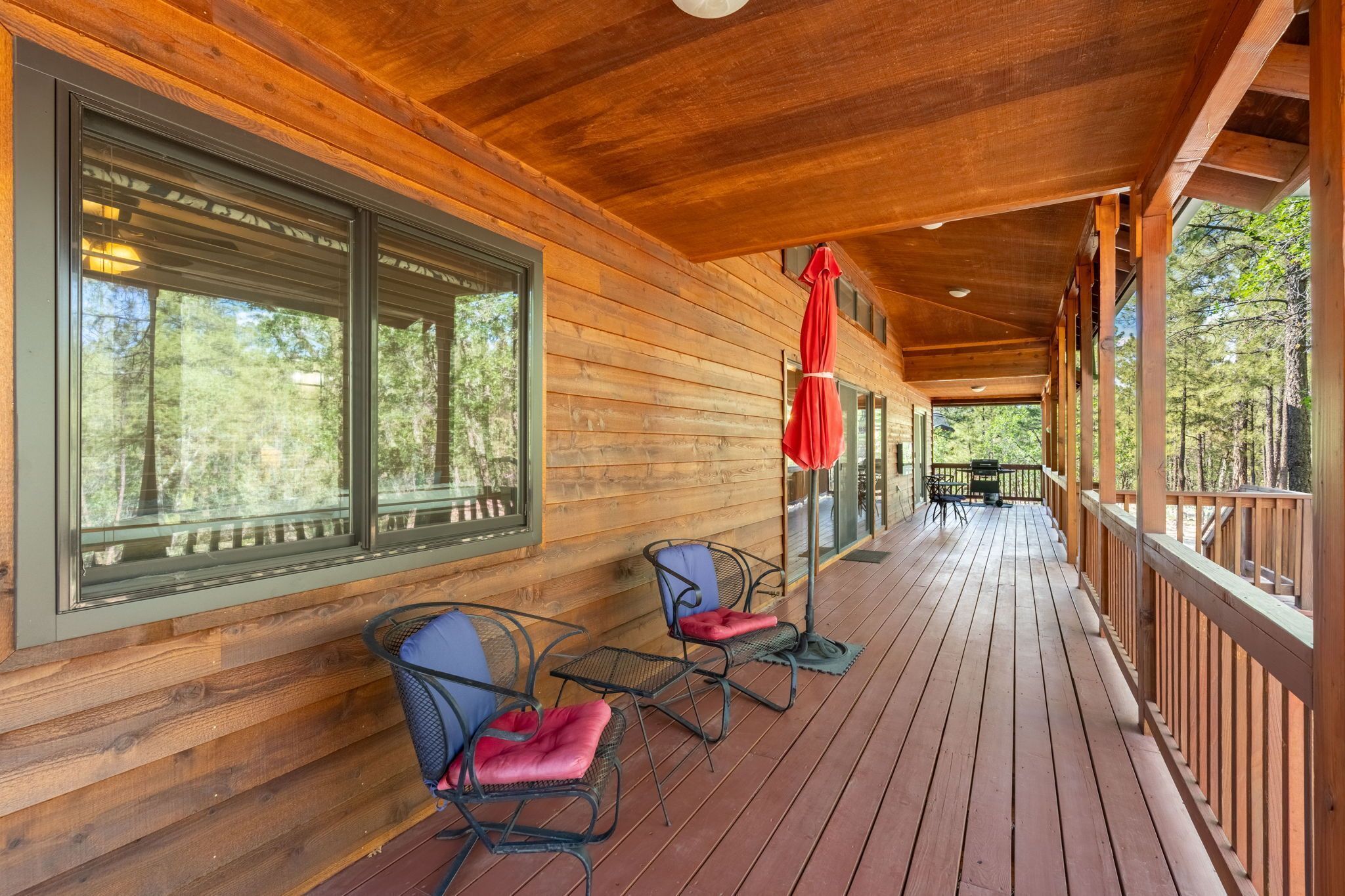 A wooden deck with chairs and a table, large windows, and a red umbrella.