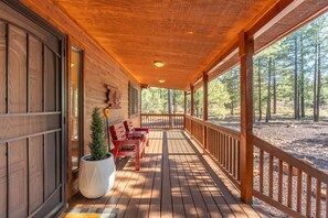 A wooden cabin with a covered porch, a small table with chairs, and a potted plant. - Mountain Retreat w/ patio | Near downtown (Show Low)