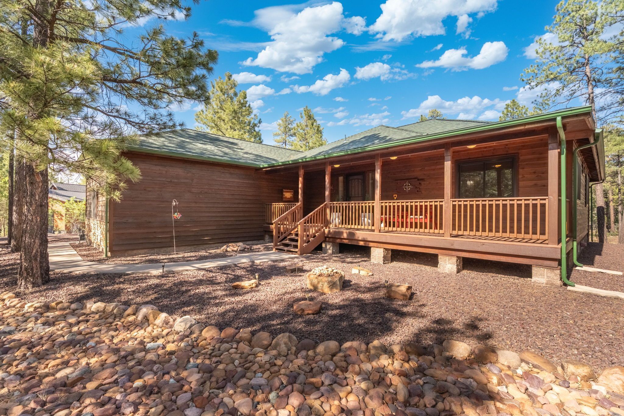 A wooden cabin with a porch, a stone pathway, and surrounding trees.