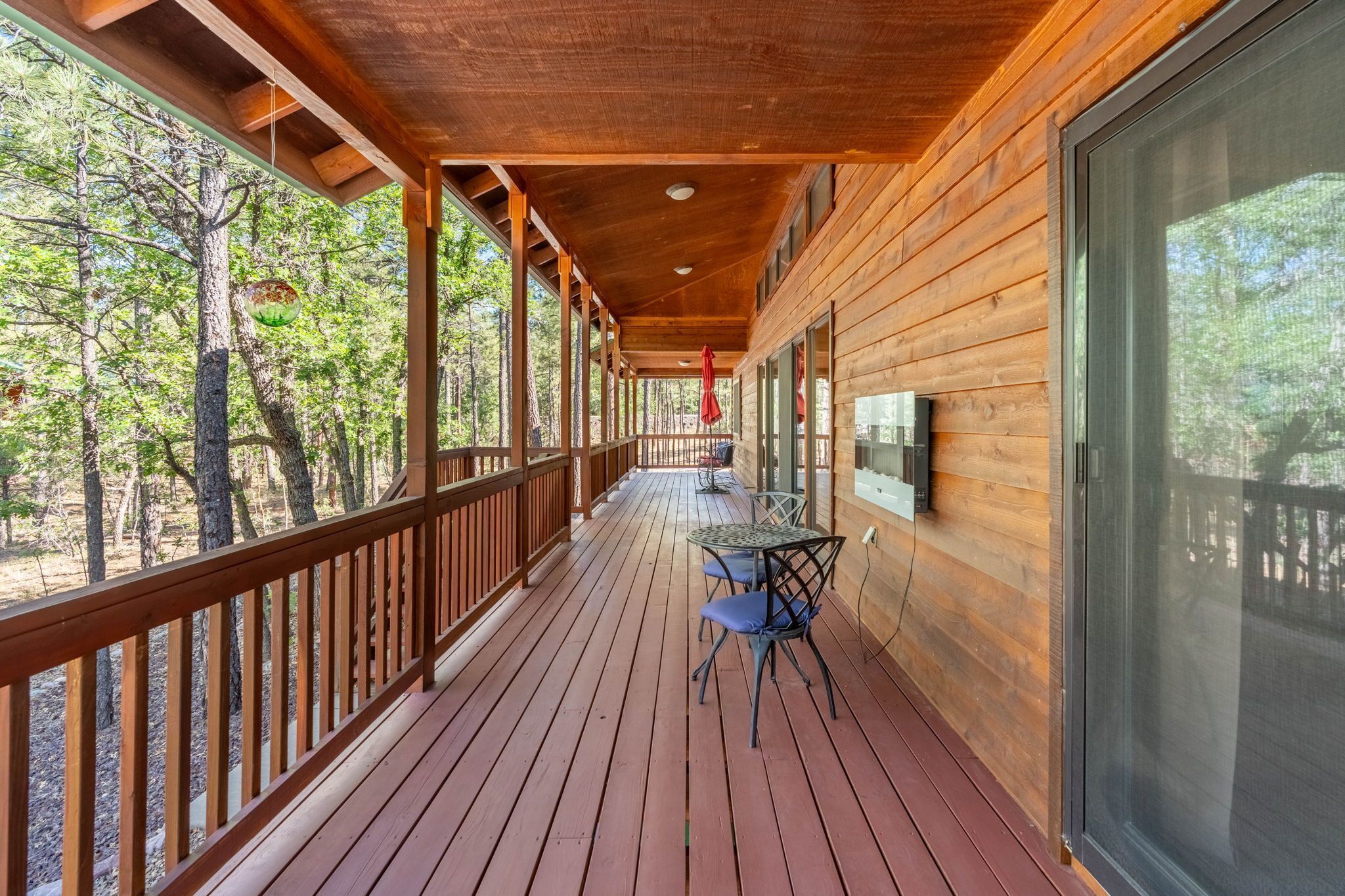 A wooden deck with a table and chairs, overlooking a forested area.
