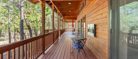 A wooden deck with a table and chairs, overlooking a forested area.