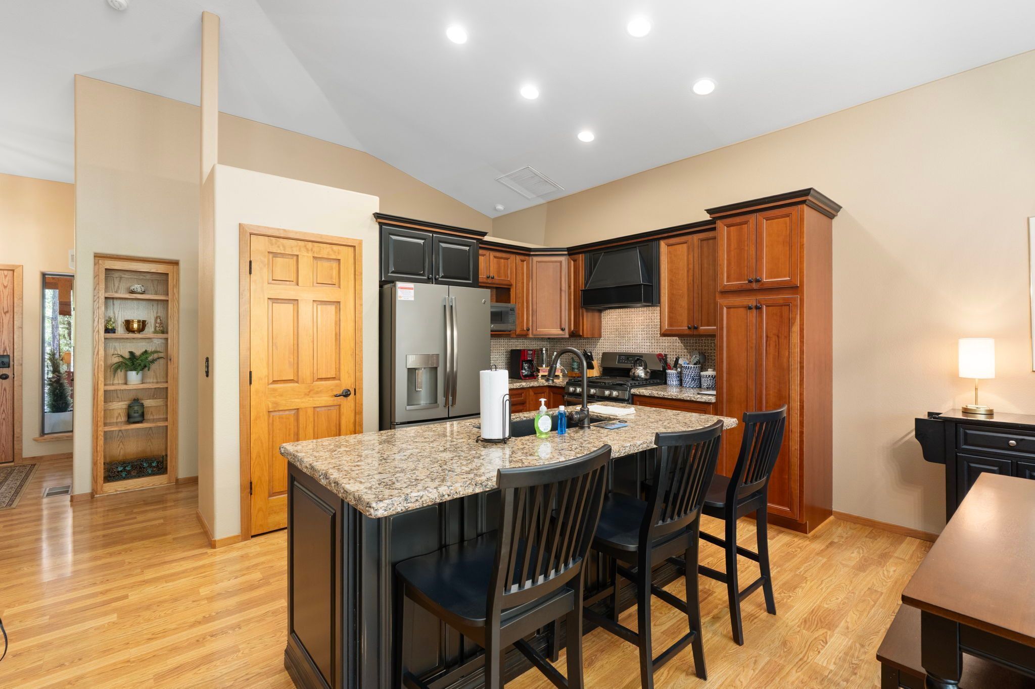 A modern kitchen with granite countertops, stainless steel appliances, wooden cabinets, and a bar area with bar stools.