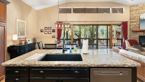 A kitchen with a granite countertop, a large island, and a dining area with a view of the outdoors.
