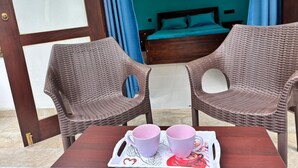 Una stanza con un letto, un tavolo con due tazze e due sedie in vimini.
