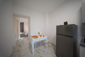 A kitchen with a white table, a stainless steel refrigerator, and a potted plant on top.