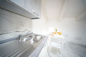 A modern kitchen with a marble countertop, stainless steel sink, and white chairs.