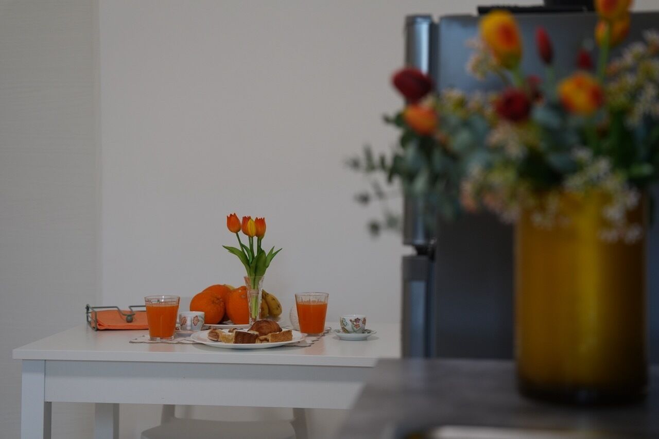 Une table de petit-déjeuner avec du jus d’orange, une assiette de nourriture et un vase de fleurs.