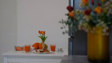 Une table de petit-déjeuner avec du jus d’orange, une assiette de nourriture et un vase de fleurs.