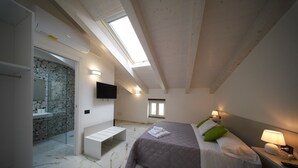 Een slaapkamer met een bed, nachtlampen, een televisie, een dakraam en een badkamer met douche en toilet.