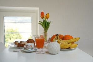A breakfast table with pastries, a glass of orange juice, a vase with tulips, and a plate of bananas and oranges.