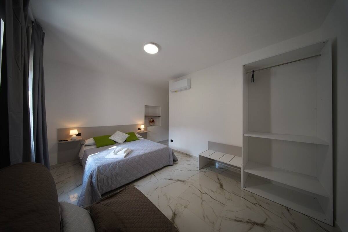 A modern hotel room with a bed, bedside tables, a bench, a wardrobe, and a ceiling light.