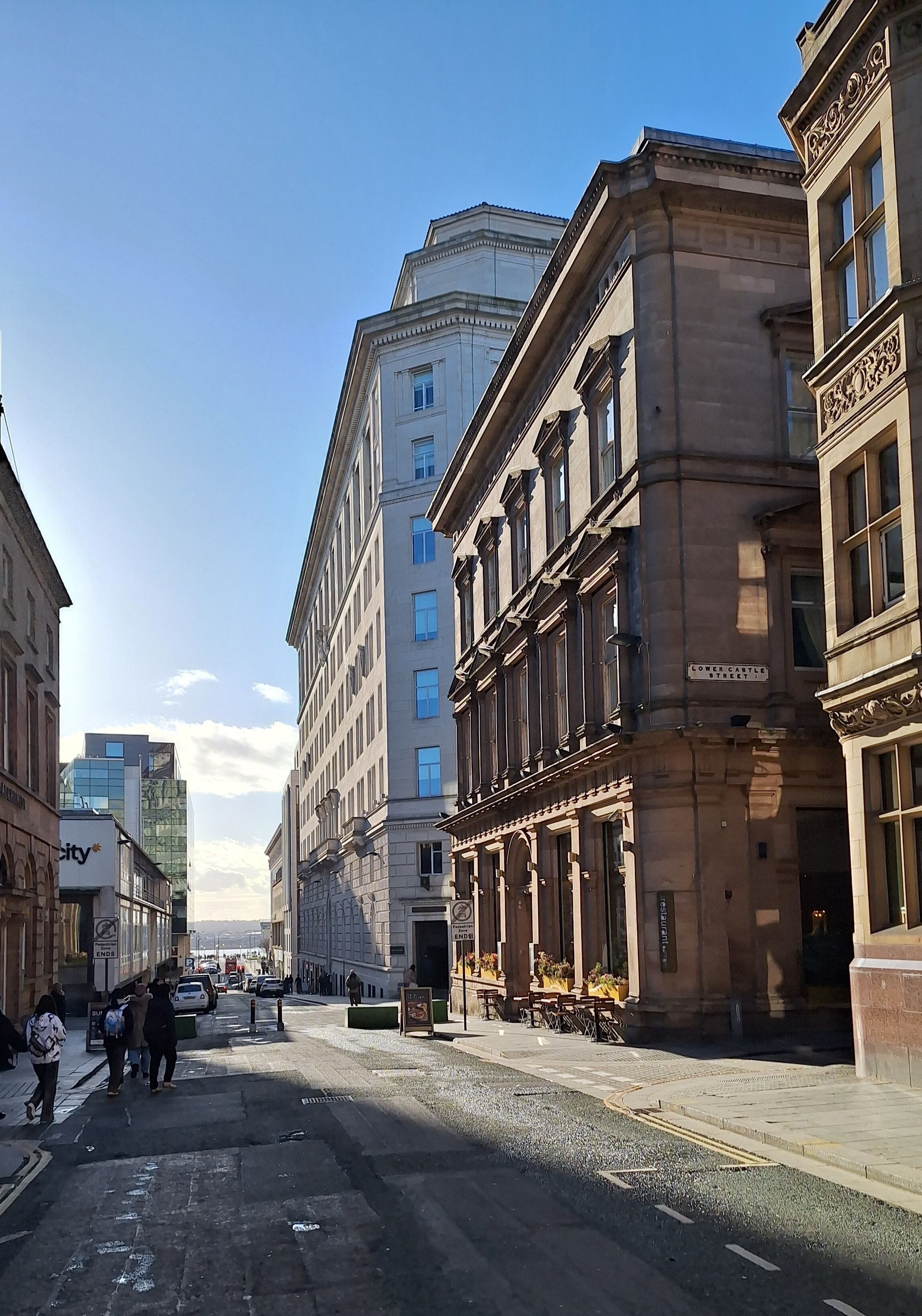 Eine Straße mit historischen Gebäuden, blauem Himmel und Fußgängern.