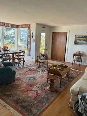A living room with a dining area, a rocking chair, a coffee table, and a view of the outdoors. - Manset oceanfront 3-bedroom home with sweeping views (Southwest Harbor)
