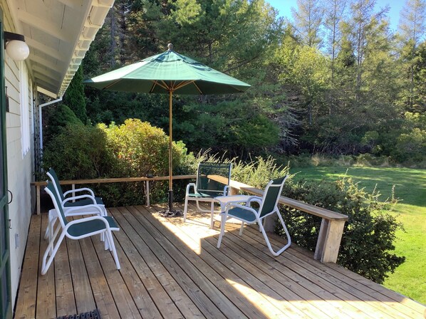 A wooden deck with outdoor furniture, including chairs and a table, under a green umbrella. - Manset oceanfront 3-bedroom home with sweeping views (Southwest Harbor)