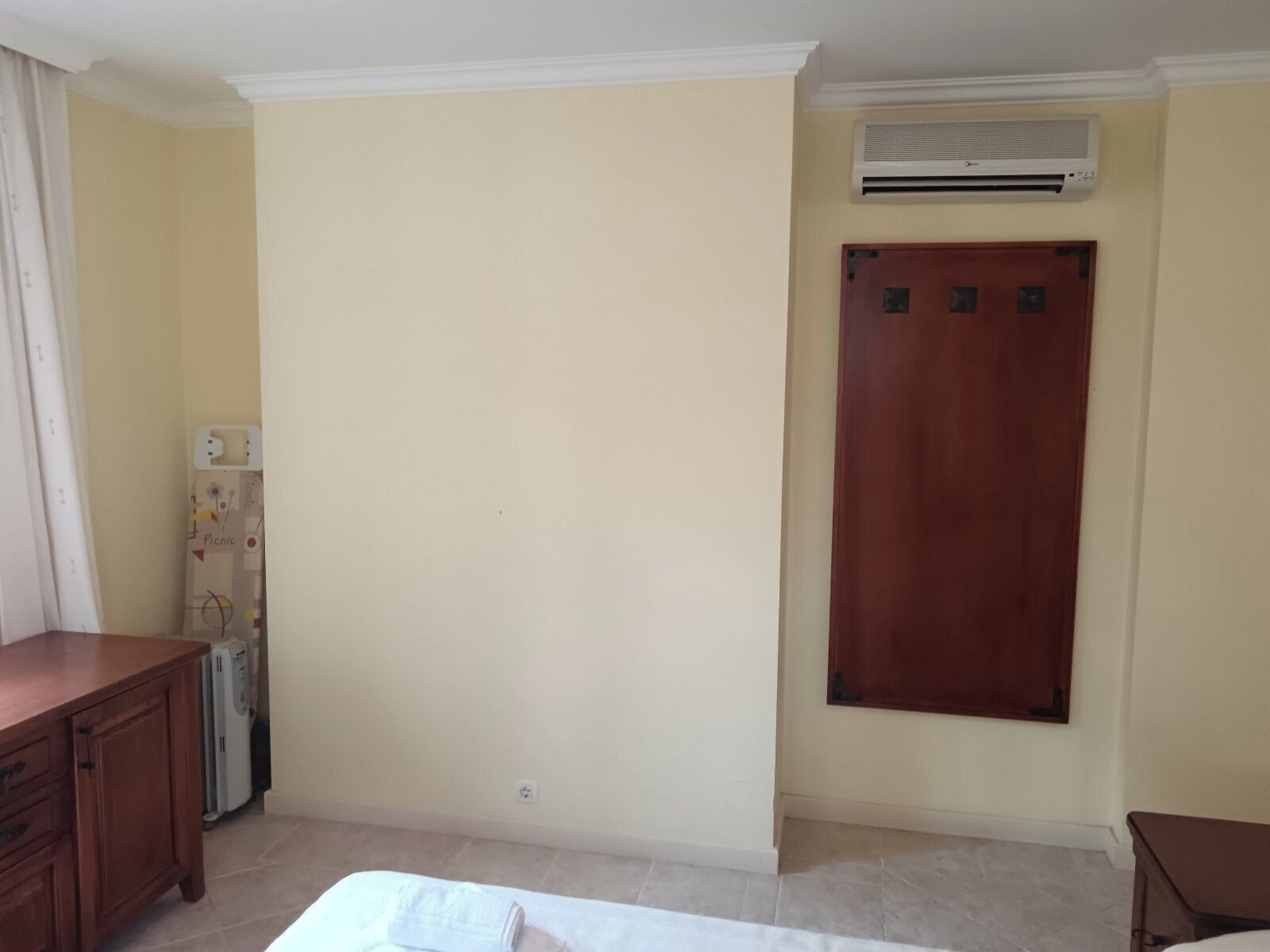 Een kamer met een houten bureau, een kledingkast, een airconditioner en een bed.