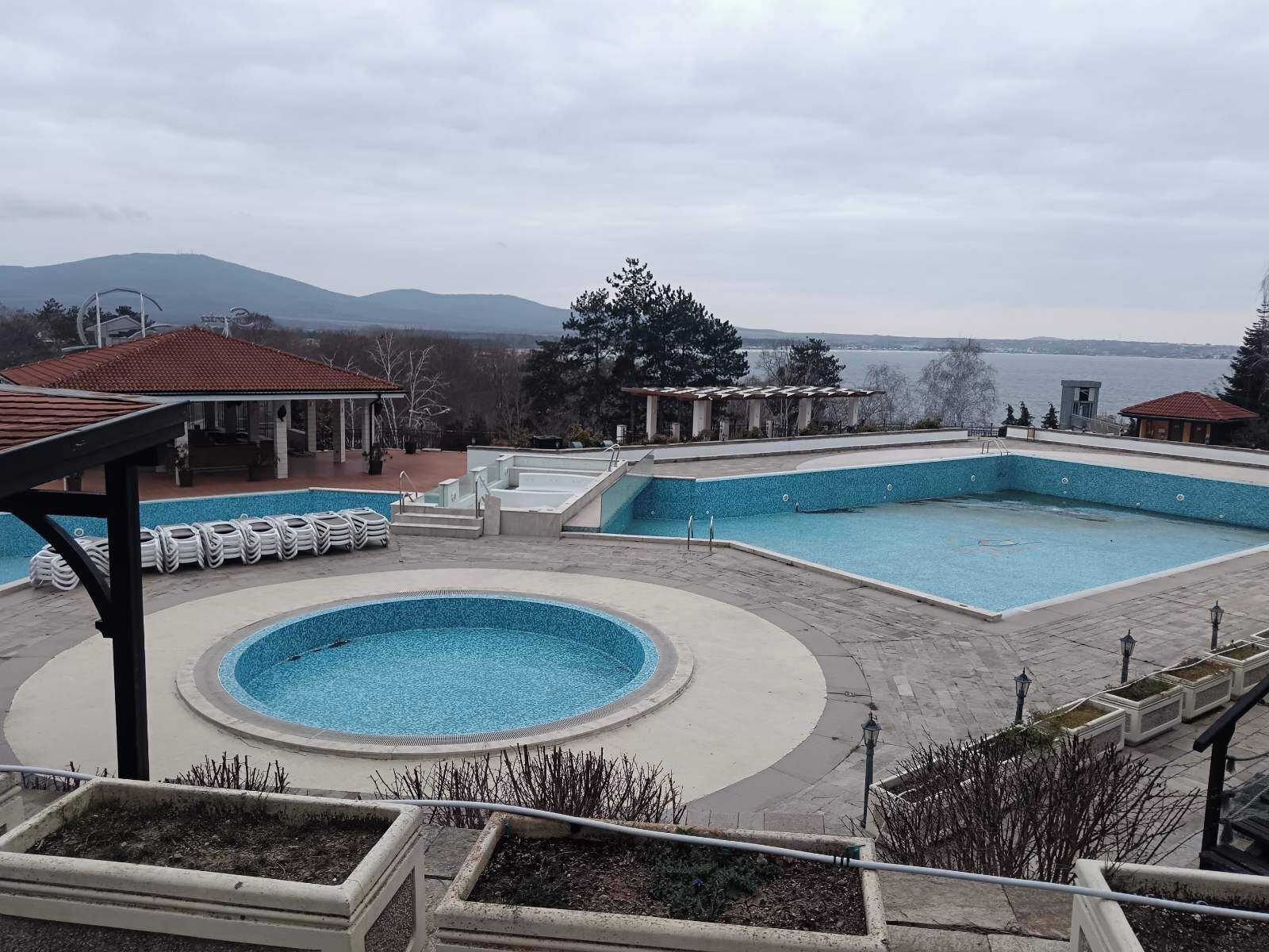 A swimming pool with a circular section, a rectangular section, and a separate hot tub area. There are lounge chairs and a covered seating area.