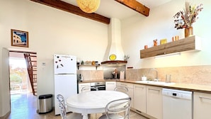 Eine moderne Küche mit einem weißen Kühlschrank, Edelstahlgeräten, einer Holzzahlendecke und einer Essecke mit weißem Tisch und Stühlen.