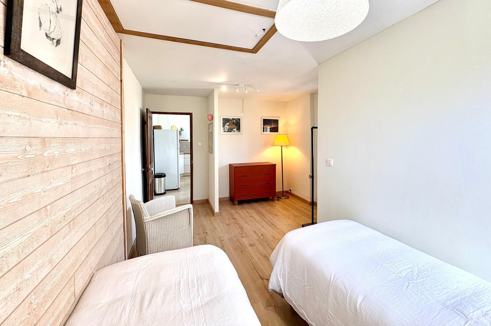 Ett rum med två sängar, en väggpanel av trä, en röd byrå, en lampa och en taklampa.