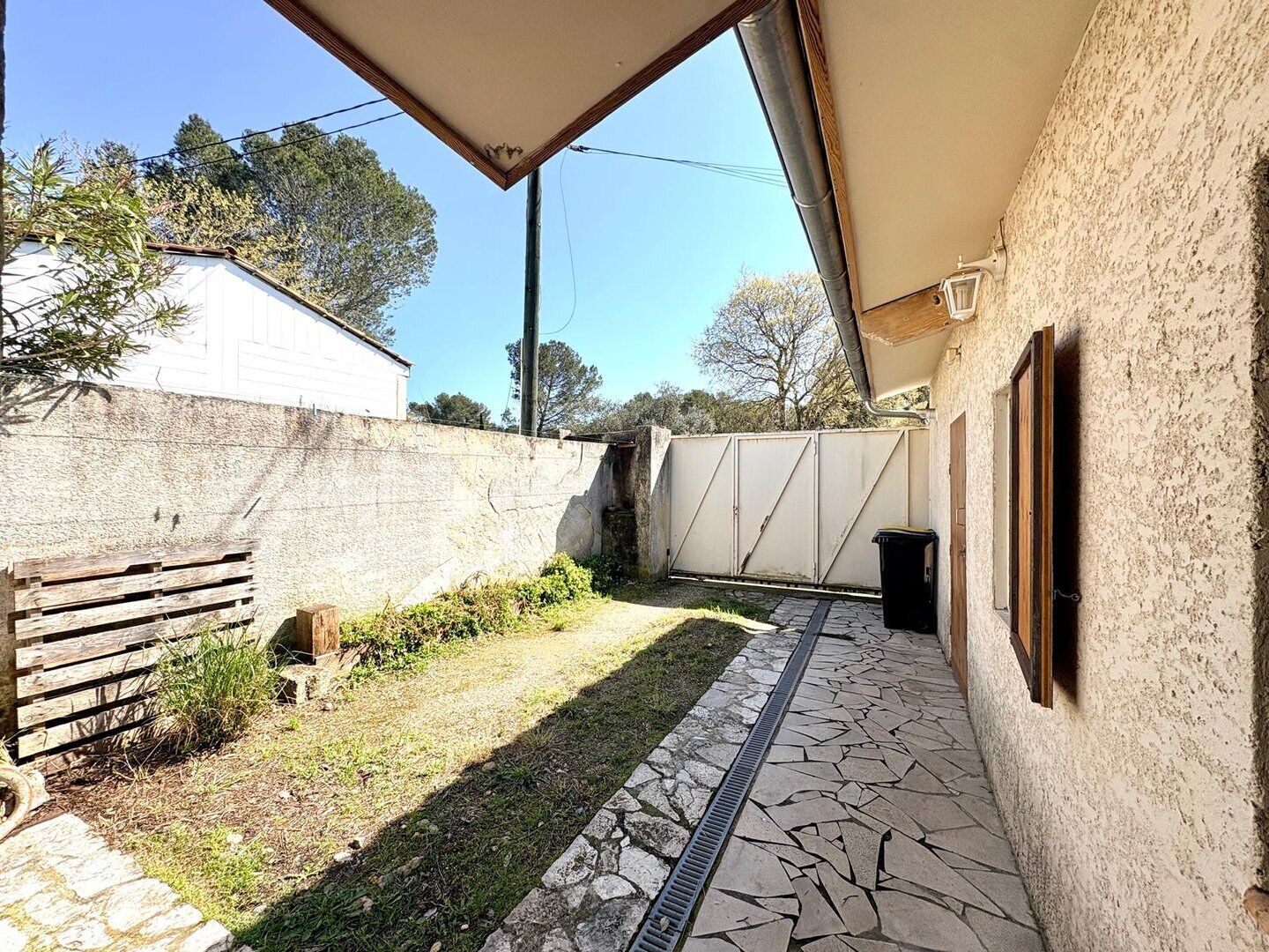 A courtyard with a stone pathway, a wooden bench, a white gate, and a wall.