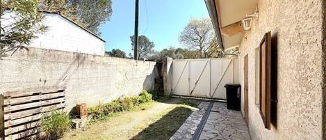 A courtyard with a stone pathway, a wooden bench, a white gate, and a wall.