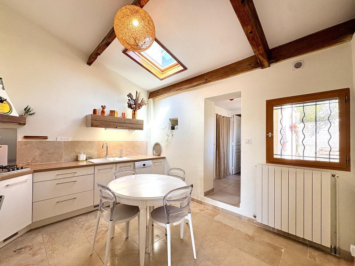 A modern kitchen with a dining table, chairs, a hanging light fixture, and a window with a view.