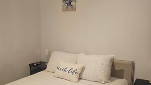 En säng med ett vitt täcke, två kuddar, ett sängbord med en lampa och två konstverk på väggen.