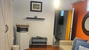 Ett vardagsrum med en soffa, ett litet bord, en mikrovågsugn, en korg, en fotoram och en tv.