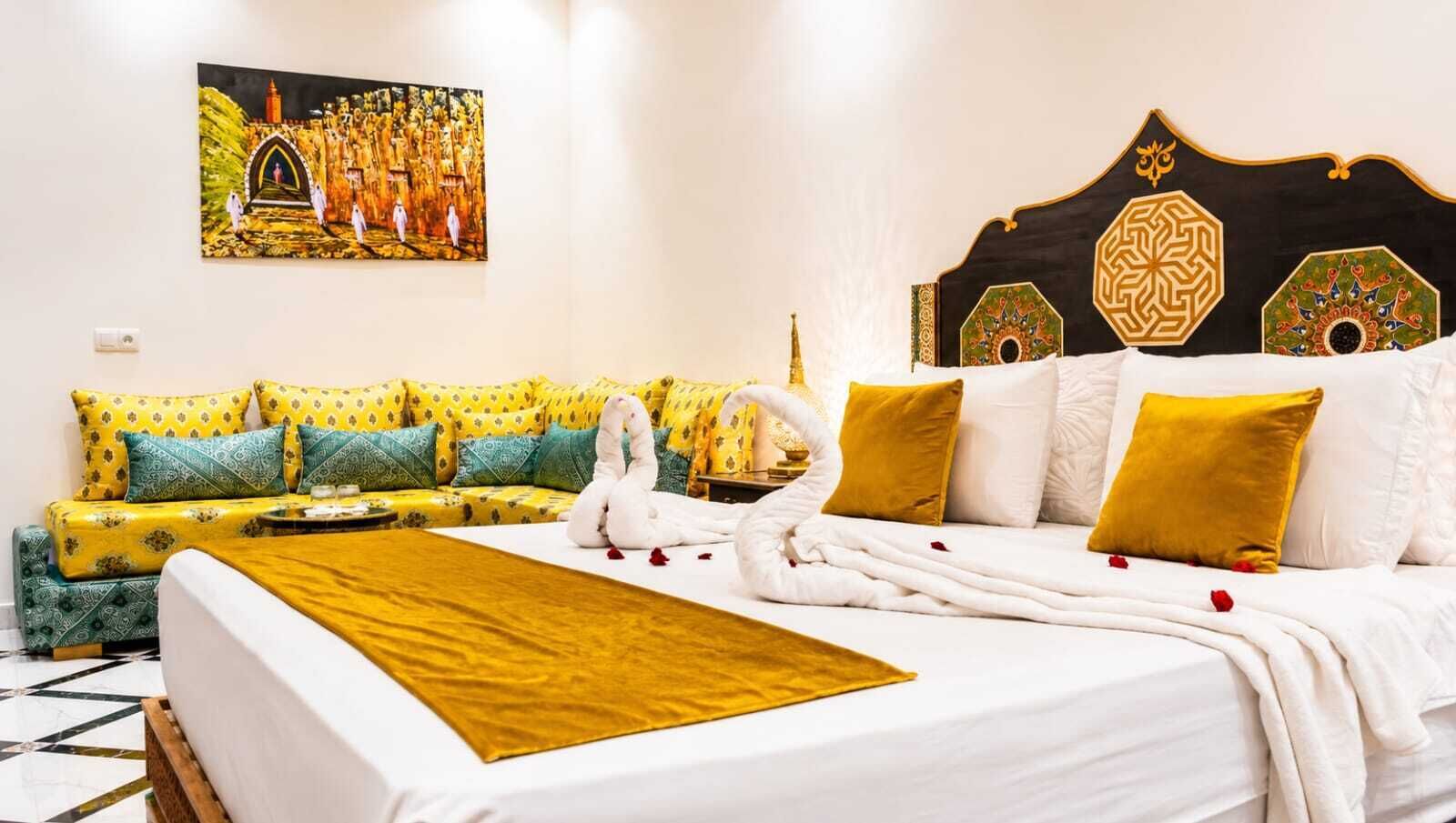 A hotel room with a bed, a sofa, a decorative headboard, and a painting on the wall.