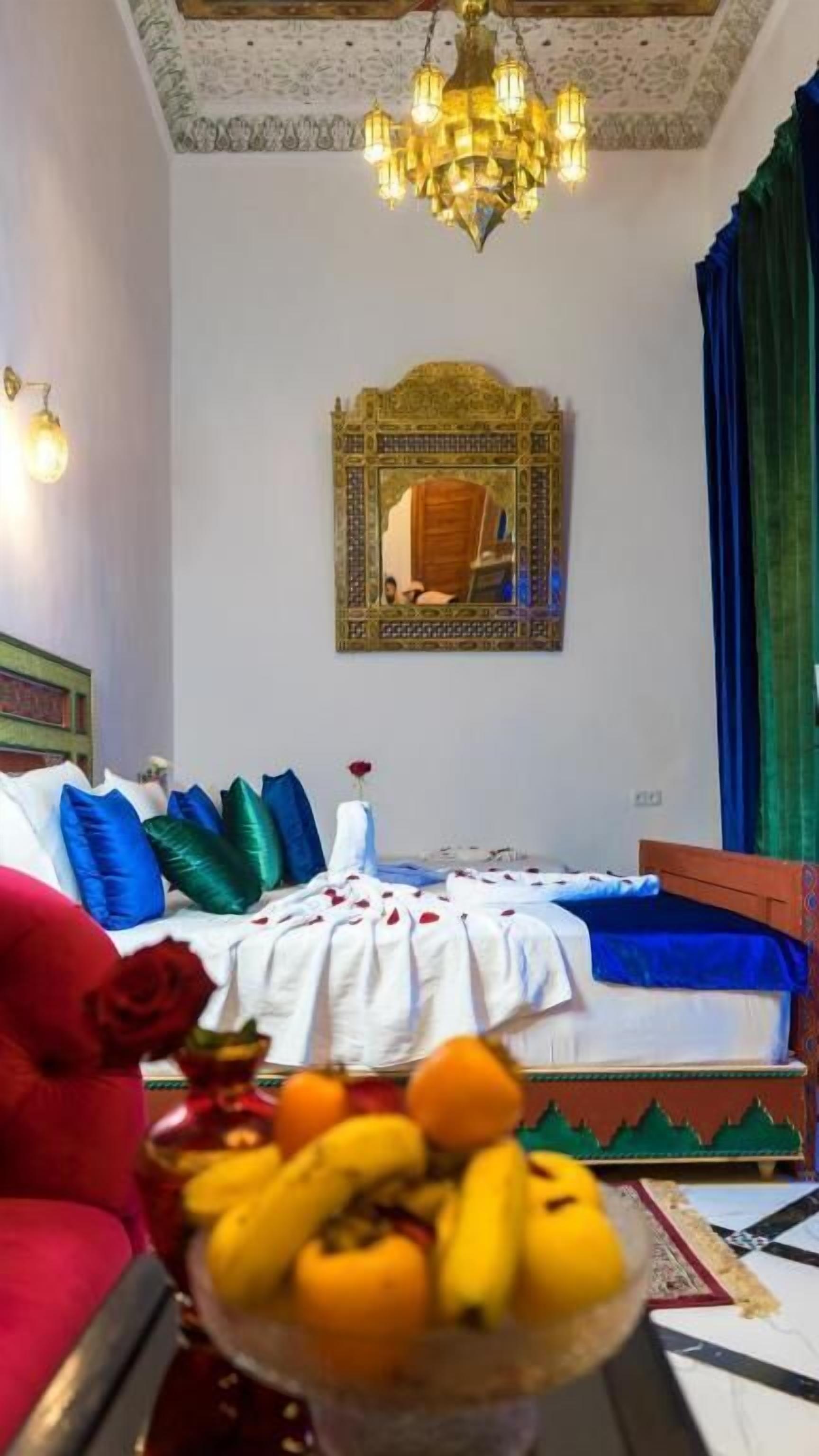A room with a bed, a chandelier, a mirror, and a bowl of fruit.