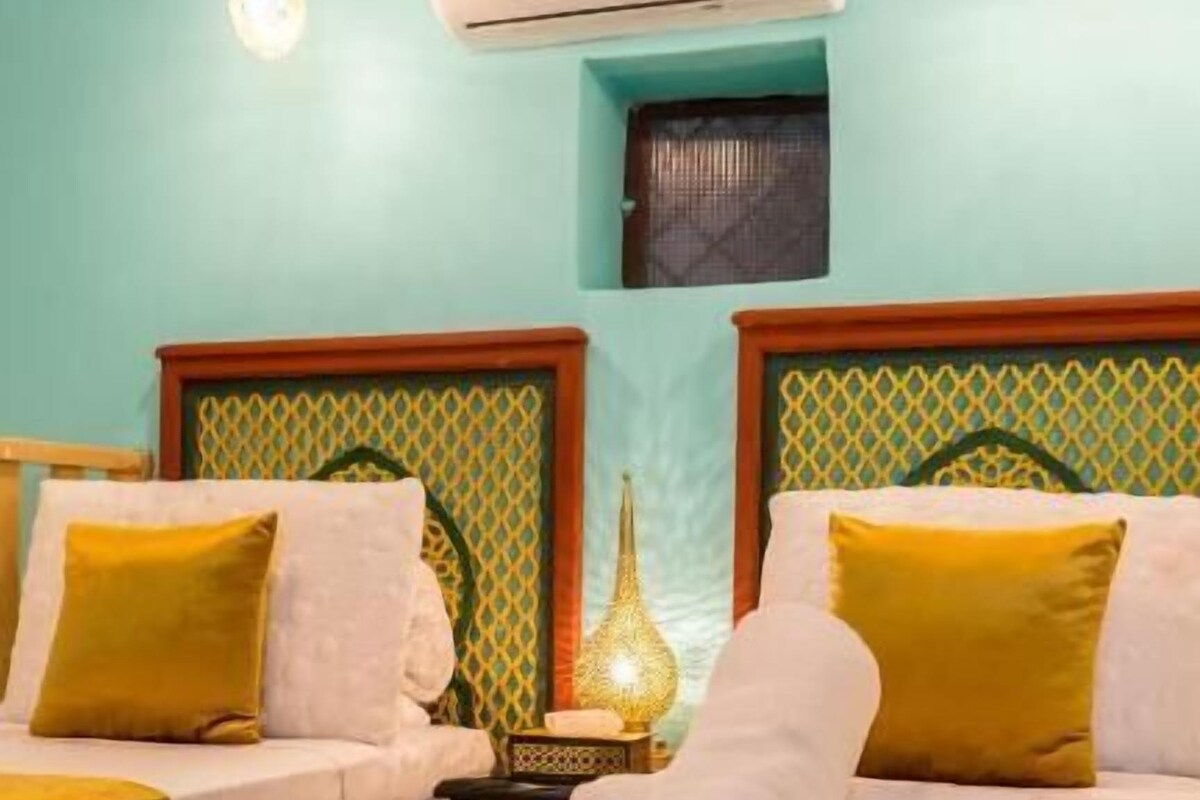 A hotel room with two beds, a wall-mounted air conditioner, a decorative lamp, and a small window.