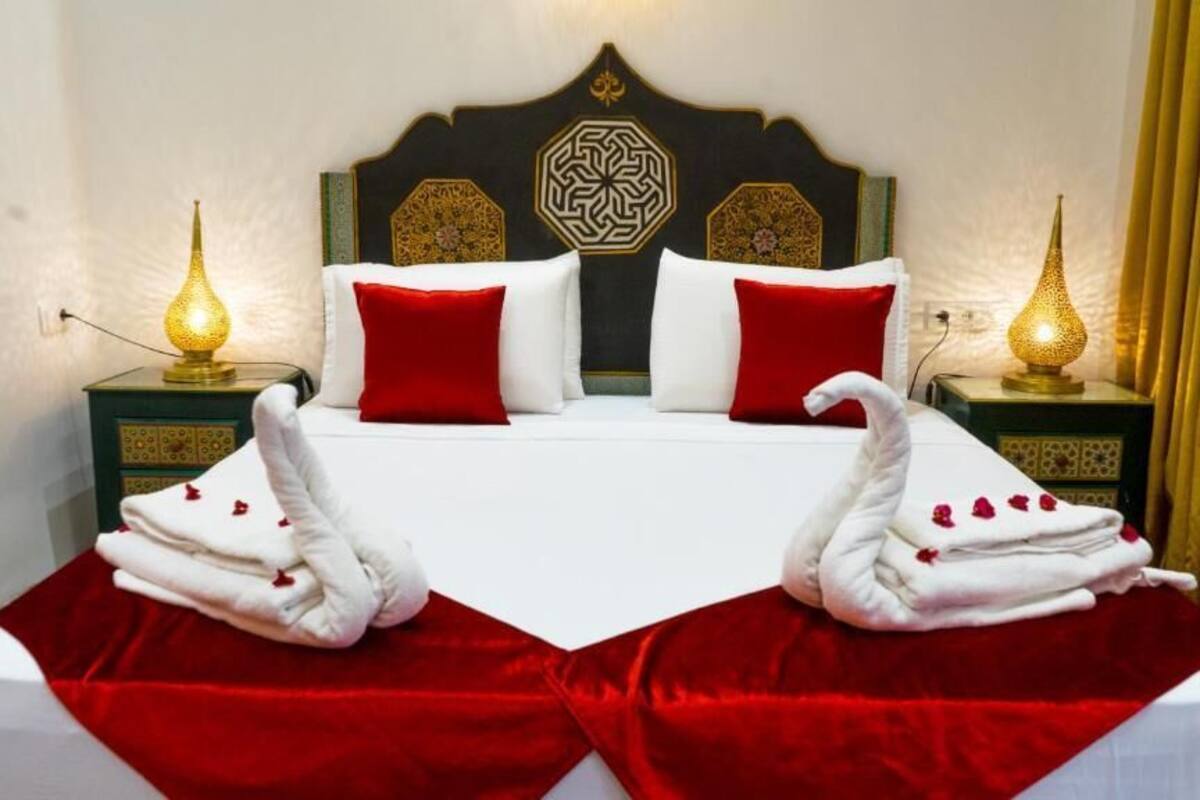 Ein Bett mit roter Bettdecke, zwei rote Kissen und zwei weiße Handtücher mit roten Rosen.