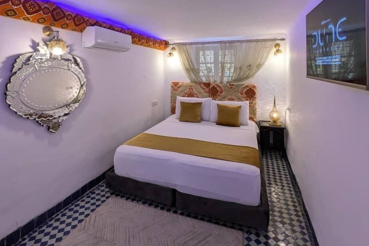 Ein Schlafzimmer mit Bett, einem dekorativen Spiegel, einem an der Wand montierten Fernseher, gemusterten Vorhängen und einem gemusterten Boden.