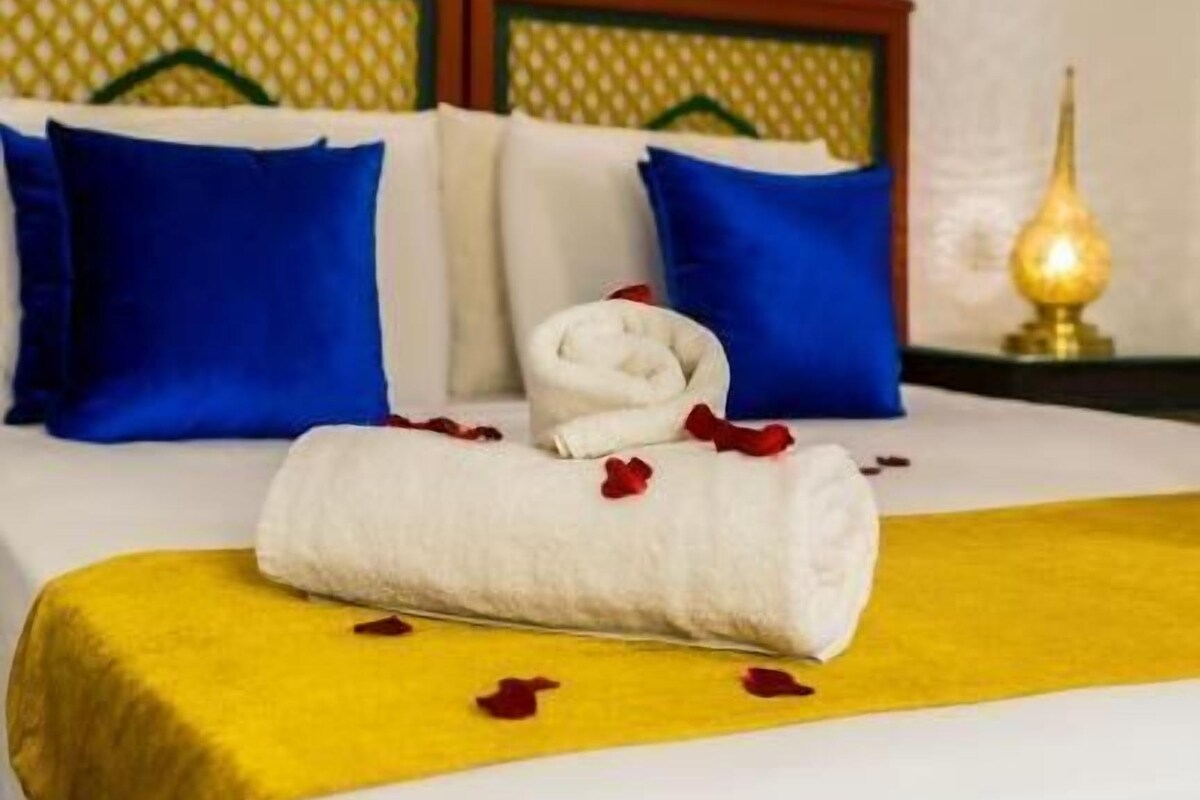 A neatly made bed with a white duvet, blue pillows, and a yellow throw blanket.