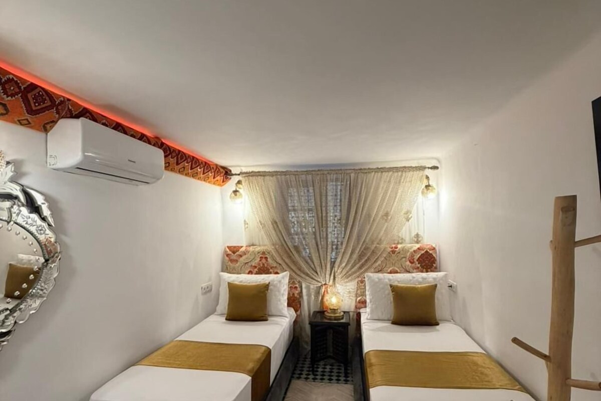 A hotel room with two beds, a checkered floor, a mirror, an air conditioner, and a wooden chair.