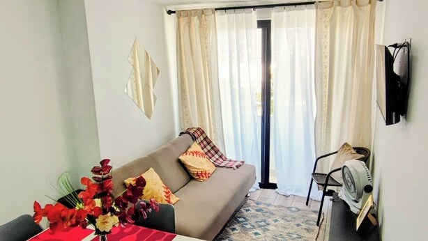 A living area with a sofa, a dining table with red placemats, a vase with flowers, and a television mounted on the wall. - Beautiful 3 bedroom apartment, Petapolis zone 12 Guatemala (Ciudad de Guatemala)