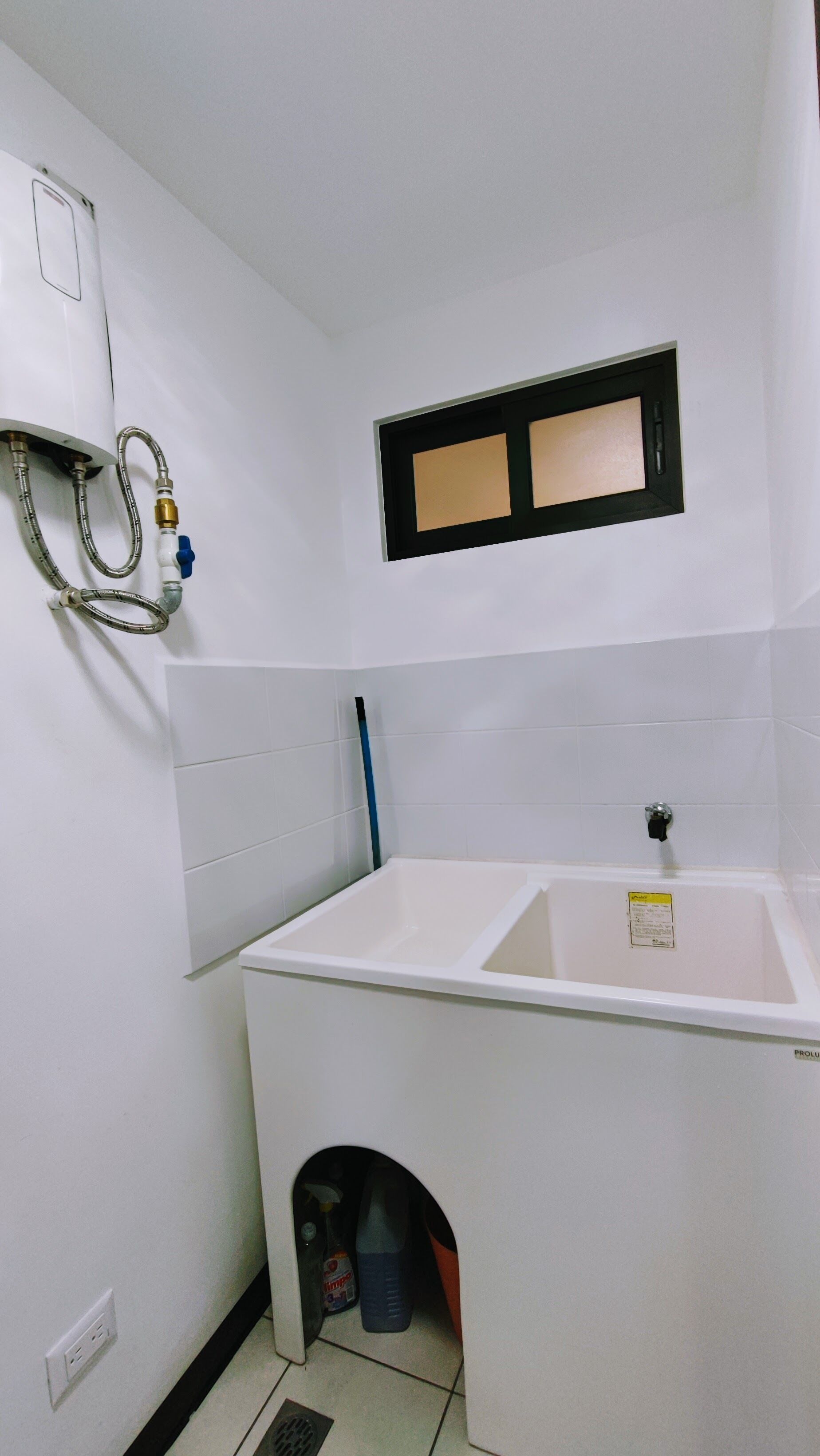 Une petite salle de bain blanche, avec un seul lavabo, une fenêtre et un espace douche.