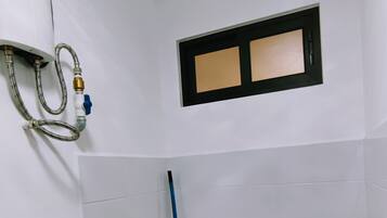 A small, white bathroom with a single sink, a window, and a shower area.