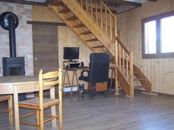 A wooden interior with a staircase, a fireplace, a desk with a computer, and a dining table with chairs.