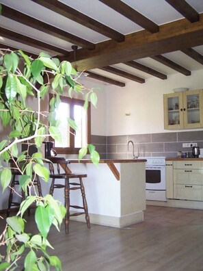 A kitchen with wooden beams, a white island with stools, a sink, and a stove.
