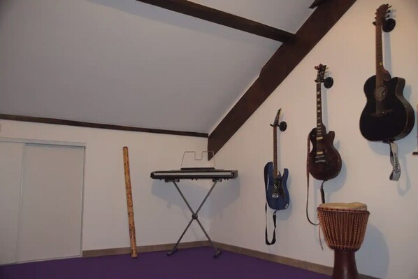A room with a purple carpet, a keyboard on a stand, and three guitars on the wall.