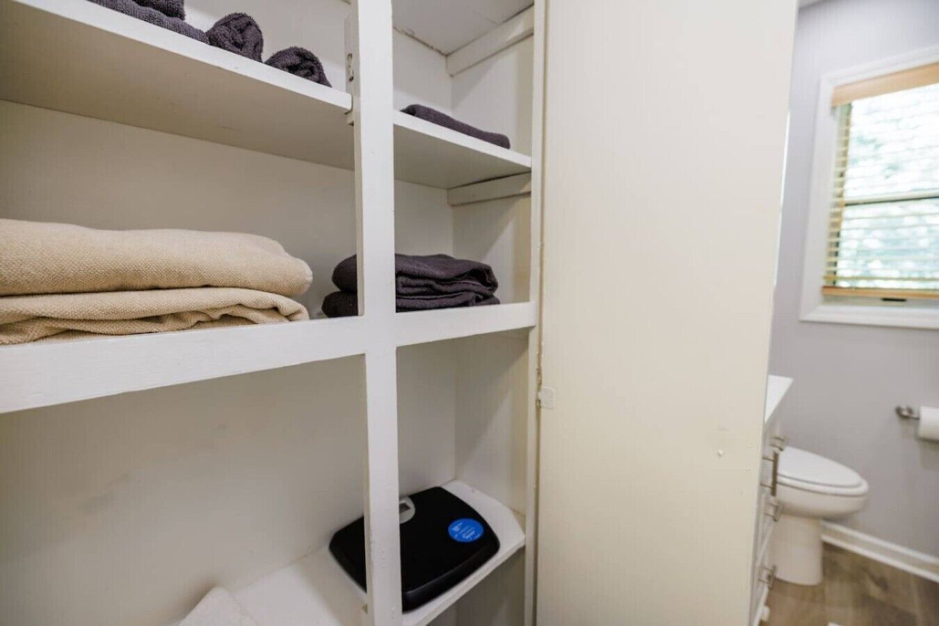 Een badkamer met een toilet, een plank met handdoeken en een weegschaal.
