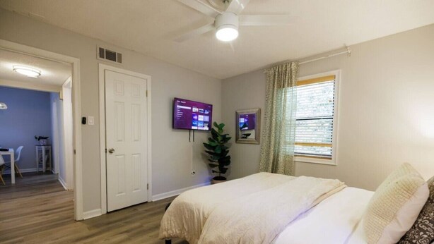 A bedroom with a bed, a television, a window with curtains, and a door leading to another room.
