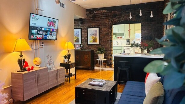 A modern living room with a flat-screen TV, wooden flooring, a blue sofa, a coffee table, and a kitchen area visible through an open doorway. - Ground floor flat at Virginia Highlands (Atlanta)