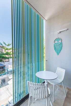 Ein Balkon mit Glastür, weißen Stühlen und einem türkisfarbenen Wandbehang aus Makramee.