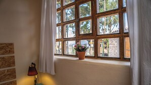 Een kamer met een raam, een blauwe nachtkastje met een lamp, en een potplant op de vensterbank.