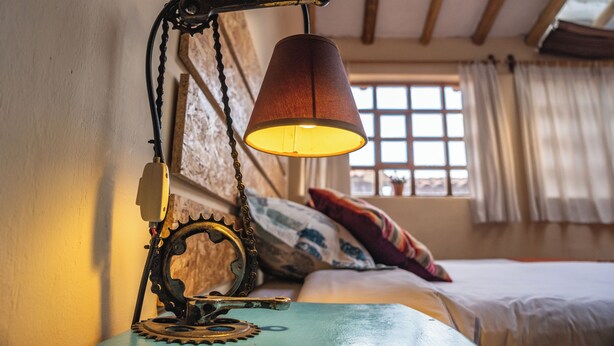 Een rustieke kamer met een bed, een raam met gordijnen en een bijzondere lamp met tandwiel en ketting.