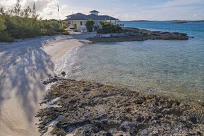 A beachfront property with a house, clear waters, and rocky shoreline.