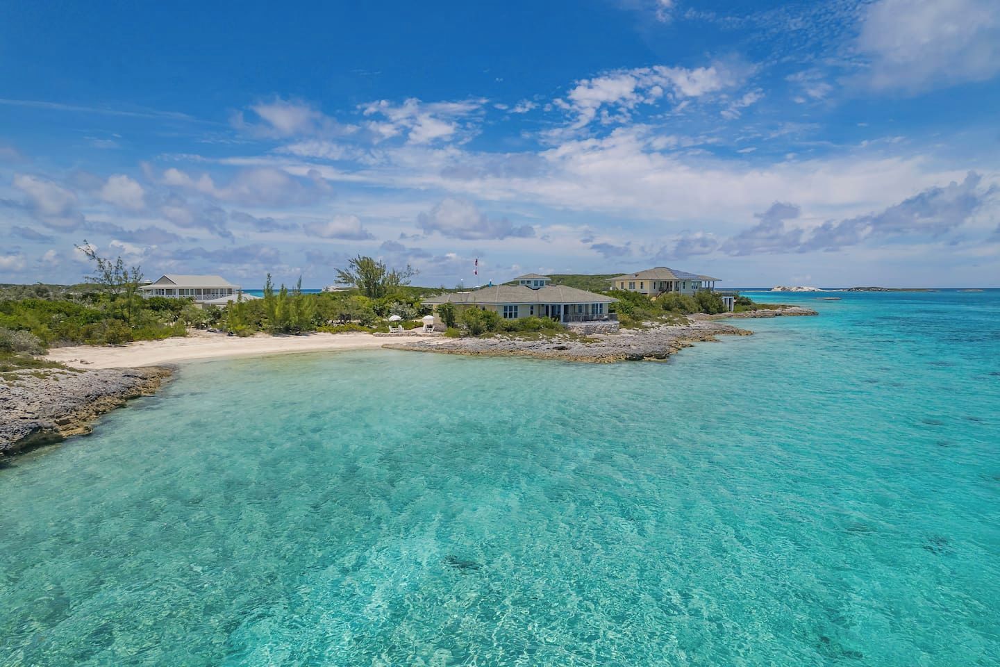 Une propriété située sur la côte, avec une eau turquoise cristalline, une plage de sable et plusieurs bâtiments dotés de grandes fenêtres donnant sur la mer.