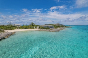 A coastal property with clear turquoise waters, a sandy beach, and several buildings with large windows overlooking the sea.