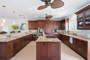 A spacious kitchen with dark wood cabinets, granite countertops, a central island, and a ceiling fan.